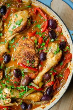 a pan filled with chicken, olives and peppers on top of a wooden table