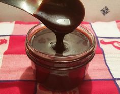 a spoon with some liquid in it on top of a glass jar filled with chocolate