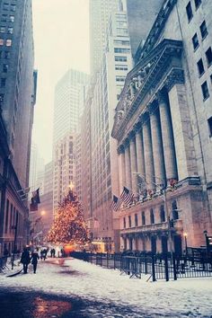 a christmas tree is in the middle of a snowy street with tall buildings behind it