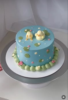 a blue cake decorated with ducks and waterlilies on a silver platter in front of a white backdrop