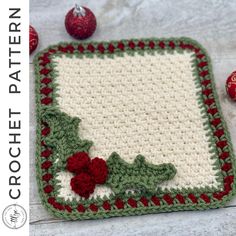 a crocheted dishcloth with holly and berries on it, next to two red balls