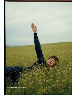 a woman laying in the middle of a field with her hand up to her head