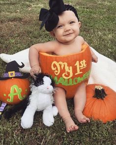 a baby sitting in a pumpkin costume next to two stuffed animals