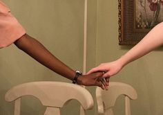 two people holding hands in front of a painting on the wall behind them is a white chair