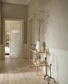 an empty hallway with white walls and wooden flooring is pictured in this image, there are two vases on the table