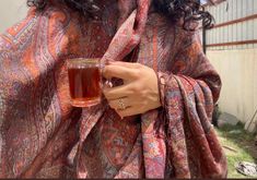 a woman wearing a shawl holding a cup of tea