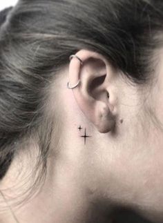 a woman's ear with a small cross tattoo on the back of her left ear