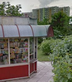 a red and white kiosk sitting on the side of a road next to trees