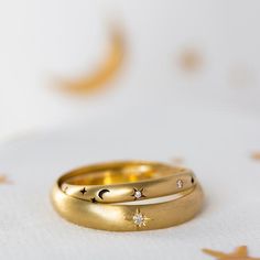 two gold wedding bands with stars and moon designs on them sitting on a white surface