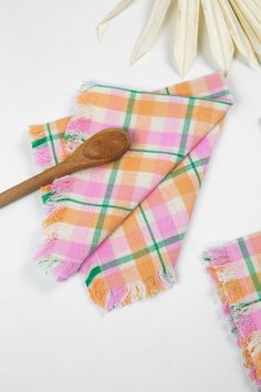 a wooden spoon sitting on top of a pink and green checkered towel next to two white toothbrushes