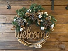 a welcome sign hanging on the side of a wooden wall with pine cones and snowflakes