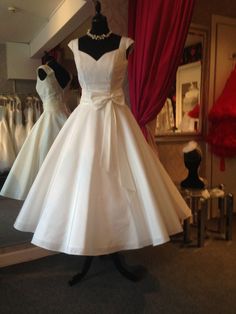 a white dress is on display in front of red curtains and mannequins