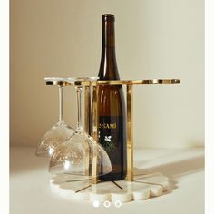 two wine glasses and a bottle in front of a gold rack with three wine glasses on it