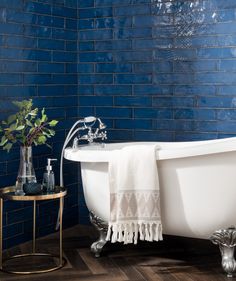 a bath tub sitting next to a wooden floor in a bathroom with blue tiles on the walls