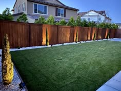 an empty backyard with grass and lights on the fence, next to a large house