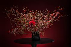 a vase filled with red flowers sitting on top of a black table covered in branches