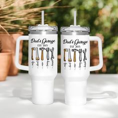 two white mugs sitting next to each other on top of a table in front of potted plants