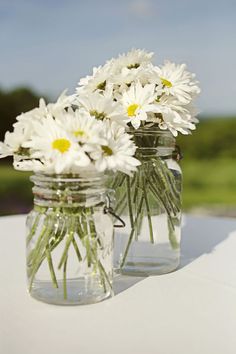 two mason jars filled with white daisies on top of a table