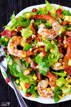 a salad with shrimp, lettuce and corn on top is served on a white plate