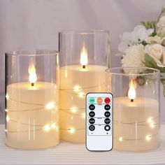 three lit candles with remote controls sitting on a table next to vases filled with flowers