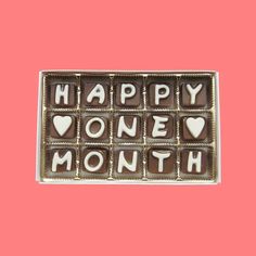 happy one month chocolates in a box on a pink background