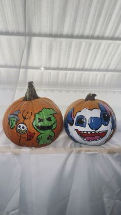 two painted pumpkins sitting on top of a white tablecloth covered surface, one with an evil clown face and the other with a skeleton