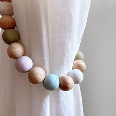 a wooden beaded necklace is hanging on a white curtain with other beads around it