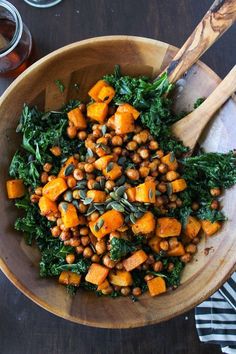 a wooden bowl filled with sweet potato and kale salad on top of a table