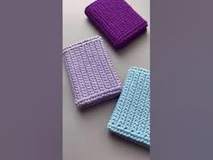 three crocheted items are sitting on a table together, one is purple and the other is blue