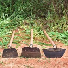 four shovels lined up in the sand with grass and bushes behind them, all on top of each other