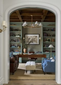 a living room with blue couches and bookshelves on the wall, along with an arched doorway leading to a sitting area