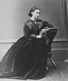 an old fashion photo of a woman in a long dress sitting on a chair with her legs crossed