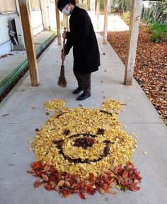 a man with a broom standing in front of a smiley face made out of leaves