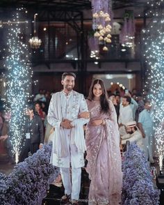 a man and woman standing next to each other in front of some purple flowers at night