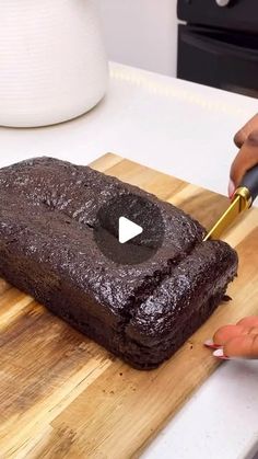 a person cutting up a chocolate cake on a wooden cutting board with a yellow knife