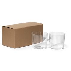 two clear glass tumblers in front of a cardboard box on a white background, one is empty