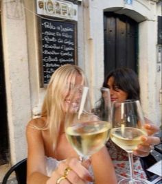 two women sitting at an outdoor table with wine glasses