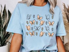 This Butterfly Flower t-shirt features delicate, soft, line art of butterflies and flowers, creating a beautiful and elegant design. Perfect for nature and gardening lovers, this tee is ideal for adding a subtle, artistic flair to any casual look. Our cute comfy Tee is crafted from soft, midweight cotton, offers versatility for effortless layering or standalone wear in the warmer months. Combining style and comfort seamlessly, we believe this tee encompasses all your wardrobe needs. Our T-shirt Blue Butterfly Print T-shirt For Spring, White Butterfly T-shirt For Spring, Butterfly Print Short Sleeve Tops For Spring, Short Sleeve Tops With Butterfly Print For Spring, Casual Butterfly Print Shirt For Spring, Spring Butterfly Graphic Print Top, Spring Butterfly Print Crew Neck Shirt, Spring Short Sleeve T-shirt With Butterfly Print, Cricut Clothing