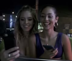 two women are smiling and looking at their cell phones