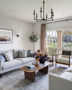 a living room filled with furniture and a chandelier hanging from the ceiling in front of a window