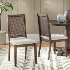 two chairs sitting on top of a rug next to a table with vases and potted plant