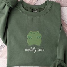 Toadally Cute Sweatshirt, Embroidered Frog Crewneck Sweater, Cute Animal Sweatshirt, Embroidered Toad Shirt, Cute Embroidered Sweatshirt  This embroidered froggy crewneck sweatshirt is everything. Perfect to show your love for frogs! ✨ 50% cotton, 50% polyester ✨ Pre-shrunk ✨ Classic fit Care: Machine wash: warm (max 40C or 105F) Tumble dry: low Do not iron directly on the print About me: My name is Sarah and I am a graduate student and music teacher! I run this small business myself and enjoy creating fun designs in my free time for some extra cash. I hope that you enjoy these designs as gifts for others or even yourself! REFUNDS AND EXCHANGES All items are made to order using multiple suppliers to ensure quick worldwide shipping. For this reason we are unable to accept returns/exchanges Casual Green Sweatshirt With Embroidery, Cute Green Embroidered Tops, Iron On Sweatshirt Ideas, Embroidered Frog, Graduate Student, Baby Boy Dress, Animal Sweatshirt, Cute Sweatshirts, Embroidered Sweater