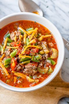 a white bowl filled with meat and vegetable soup on top of a wooden cutting board