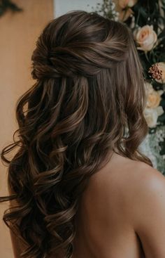 the back of a woman's head with long, wavy hair and flowers in the background