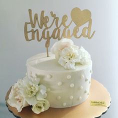 there is a white cake with flowers on the top that says we're engaged