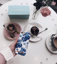 a person holding an iphone in front of a table with coffee and cakes on it