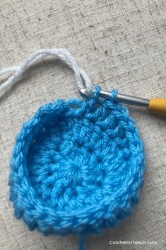 a crocheted blue object is next to a knitting needle on a piece of fabric