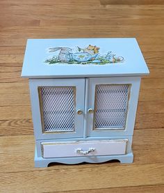 a small blue cabinet with glass doors on the top and bottom, sitting on a wooden floor