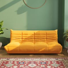 a yellow futon sofa sitting on top of a rug in front of a green wall