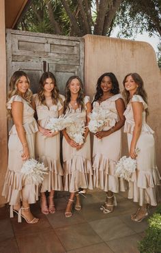 a group of women standing next to each other wearing dresses and holding bouquets in their hands